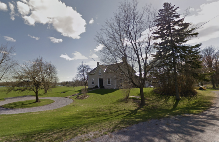 A beautiful modest historic stone farmhouse. It is made of limestone, 1 and a half stories, with a central door, dormer above and a window on either side. The house sits ona grassy knoll with some trees around.