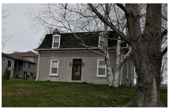 Mid 19th-century limestone house. Central door with a window on either side, and a mansard roof with two windows directly above those.