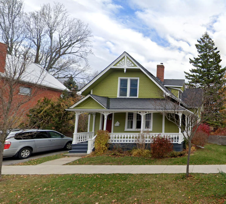 This rare surviving example of a late 19th century vernacular Carpenter Gothic frame house has intricate white dental work, a wrap around porch and green siding